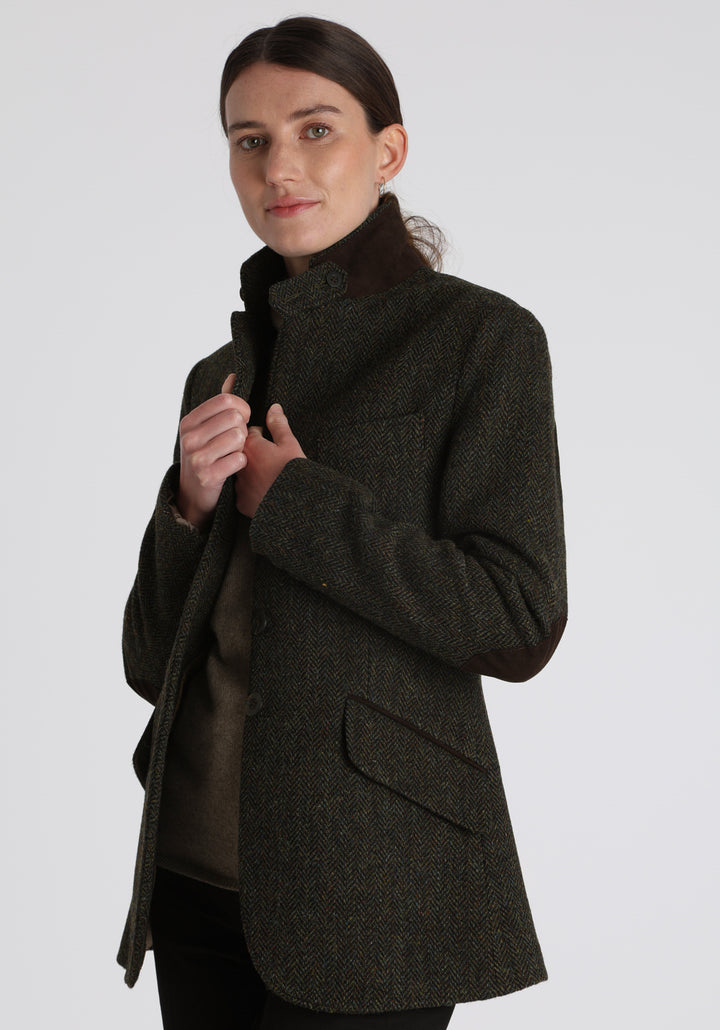 Model wearing the Patmos waistcoat in green spruce herringbone Harris Tweed with suede trim, a longline, neatly tailored style with a mandarin collar.