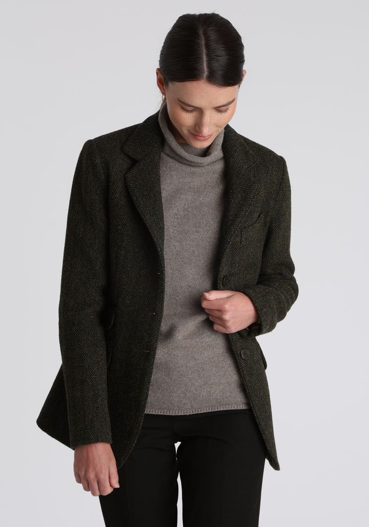 Model wearing the Patmos waistcoat in green spruce herringbone Harris Tweed with suede trim, a longline, neatly tailored style with a mandarin collar.