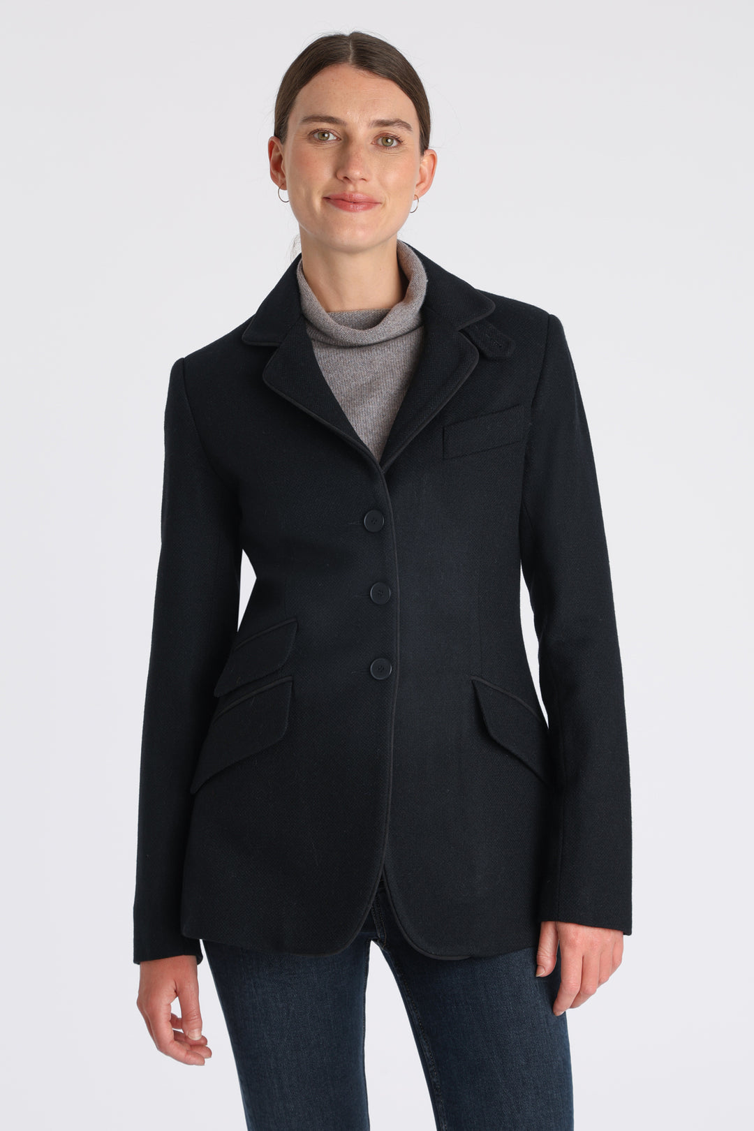 Model wearing the Cass jacket in blue spruce herringbone Harris Tweed with suede trim, a longline, relaxed boyfriend-style jacket with welt pockets, and buttoned collar tab inspired by equestrian tailoring.