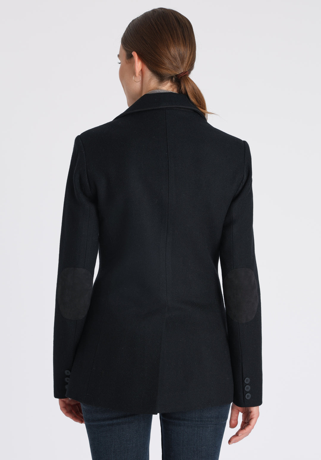 Model wearing the Cass jacket in blue spruce herringbone Harris Tweed with suede trim, a longline, relaxed boyfriend-style jacket with welt pockets, and buttoned collar tab inspired by equestrian tailoring.