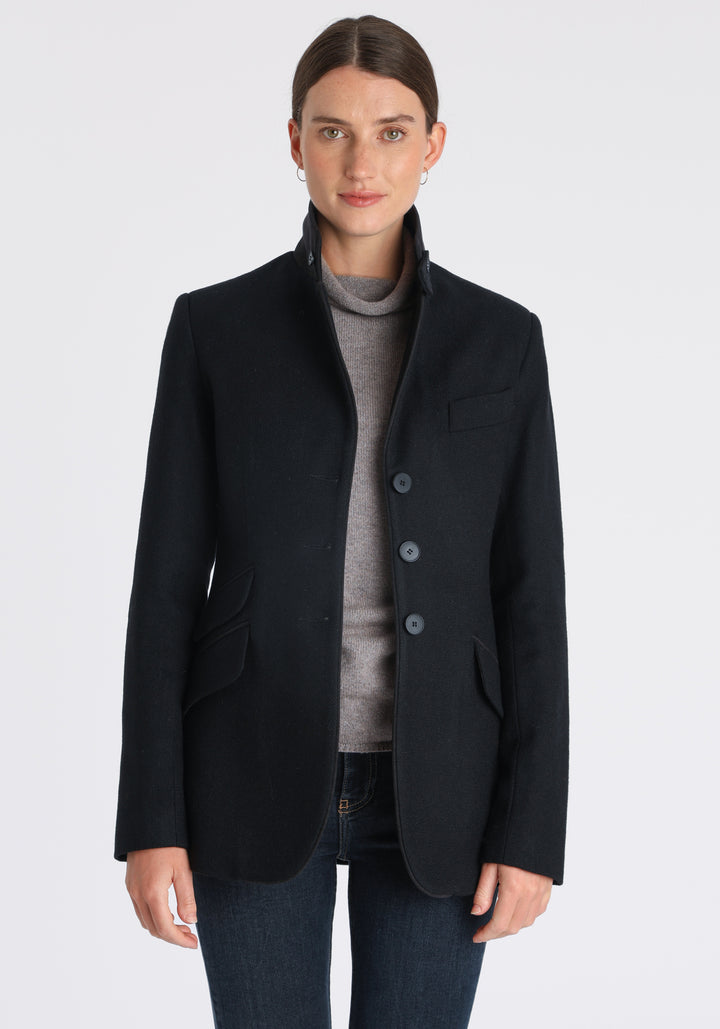 Model wearing the Cass jacket in blue spruce herringbone Harris Tweed with suede trim, a longline, relaxed boyfriend-style jacket with welt pockets, and buttoned collar tab inspired by equestrian tailoring.