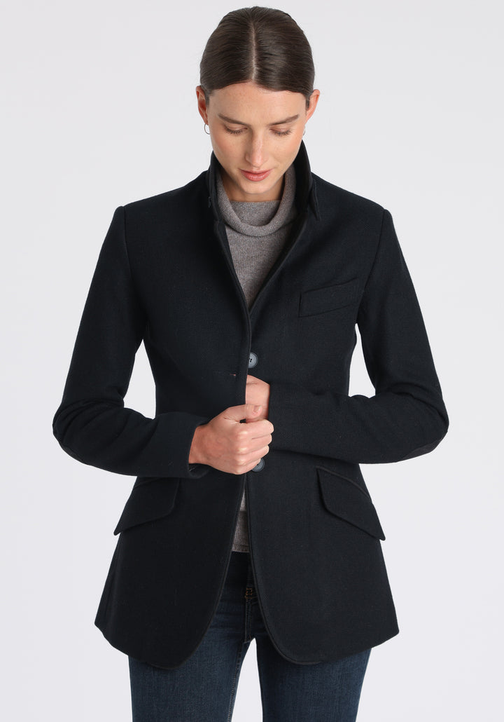 Model wearing the Cass jacket in blue spruce herringbone Harris Tweed with suede trim, a longline, relaxed boyfriend-style jacket with welt pockets, and buttoned collar tab inspired by equestrian tailoring.