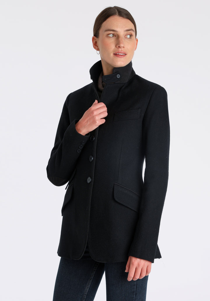 Model wearing the Cass jacket in blue spruce herringbone Harris Tweed with suede trim, a longline, relaxed boyfriend-style jacket with welt pockets, and buttoned collar tab inspired by equestrian tailoring.