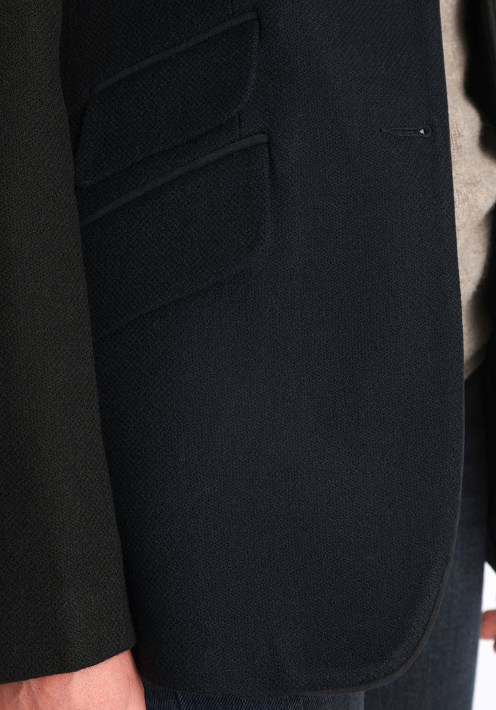 Model wearing the Cass jacket in blue spruce herringbone Harris Tweed with suede trim, a longline, relaxed boyfriend-style jacket with welt pockets, and buttoned collar tab inspired by equestrian tailoring.