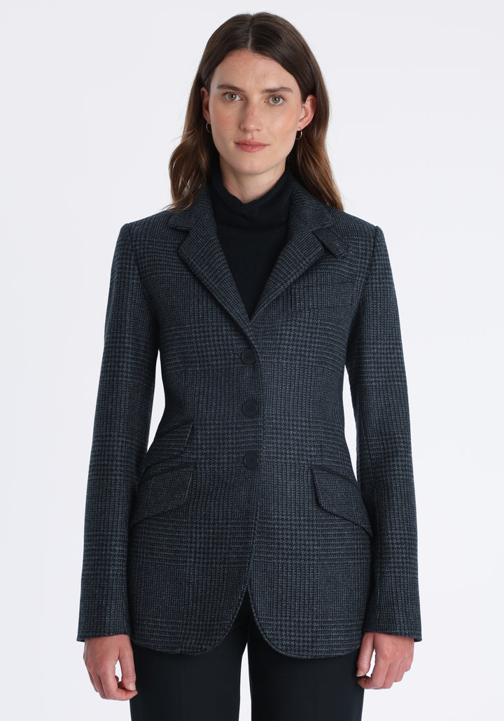 Model wearing the Cass jacket in black and charcoal grey Prince of Wales wool check with suede trim, a longline, relaxed boyfriend-style jacket with welt pockets, and buttoned collar tab inspired by equestrian tailoring.