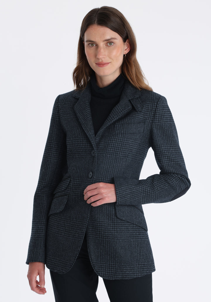 Model wearing the Cass jacket in black and charcoal grey Prince of Wales wool check with suede trim, a longline, relaxed boyfriend-style jacket with welt pockets, and buttoned collar tab inspired by equestrian tailoring.