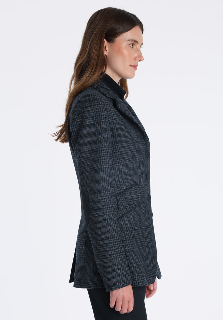 Model wearing the Cass jacket in black and charcoal grey Prince of Wales wool check with suede trim, a longline, relaxed boyfriend-style jacket with welt pockets, and buttoned collar tab inspired by equestrian tailoring.