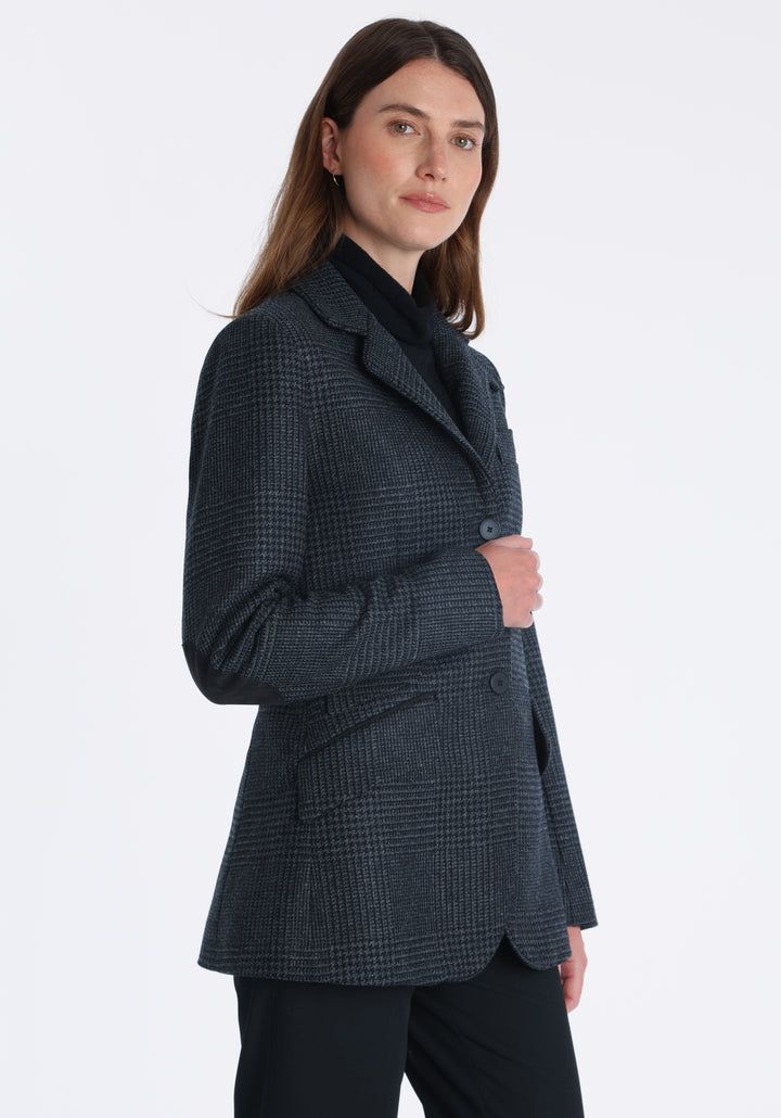 Model wearing the Cass jacket in black and charcoal grey Prince of Wales wool check with suede trim, a longline, relaxed boyfriend-style jacket with welt pockets, and buttoned collar tab inspired by equestrian tailoring.