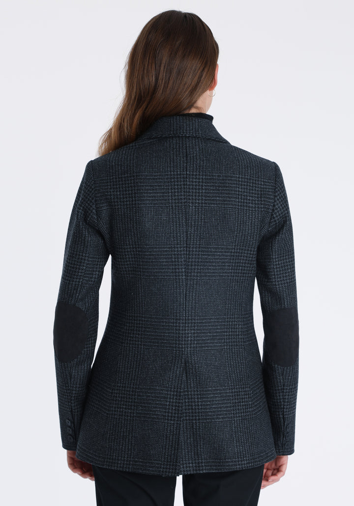 Model wearing the Cass jacket in black and charcoal grey Prince of Wales wool check with suede trim, a longline, relaxed boyfriend-style jacket with welt pockets, and buttoned collar tab inspired by equestrian tailoring.