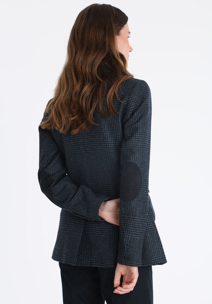 Model wearing the Cass jacket in black and charcoal grey Prince of Wales wool check with suede trim, a longline, relaxed boyfriend-style jacket with welt pockets, and buttoned collar tab inspired by equestrian tailoring.