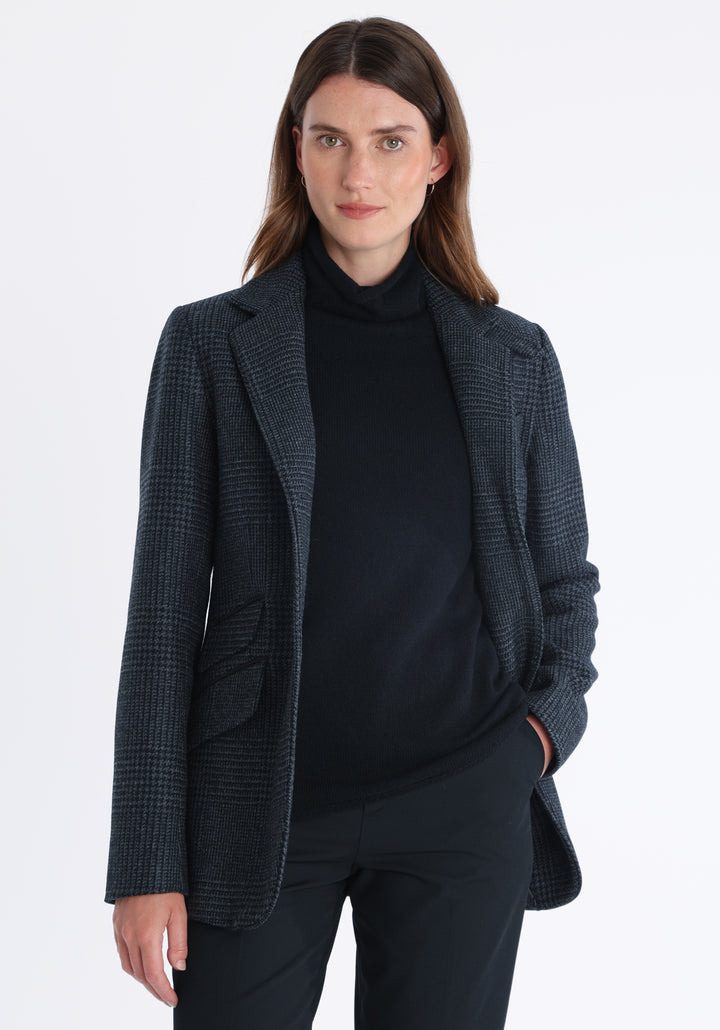 Model wearing the Cass jacket in black and charcoal grey Prince of Wales wool check with suede trim, a longline, relaxed boyfriend-style jacket with welt pockets, and buttoned collar tab inspired by equestrian tailoring.