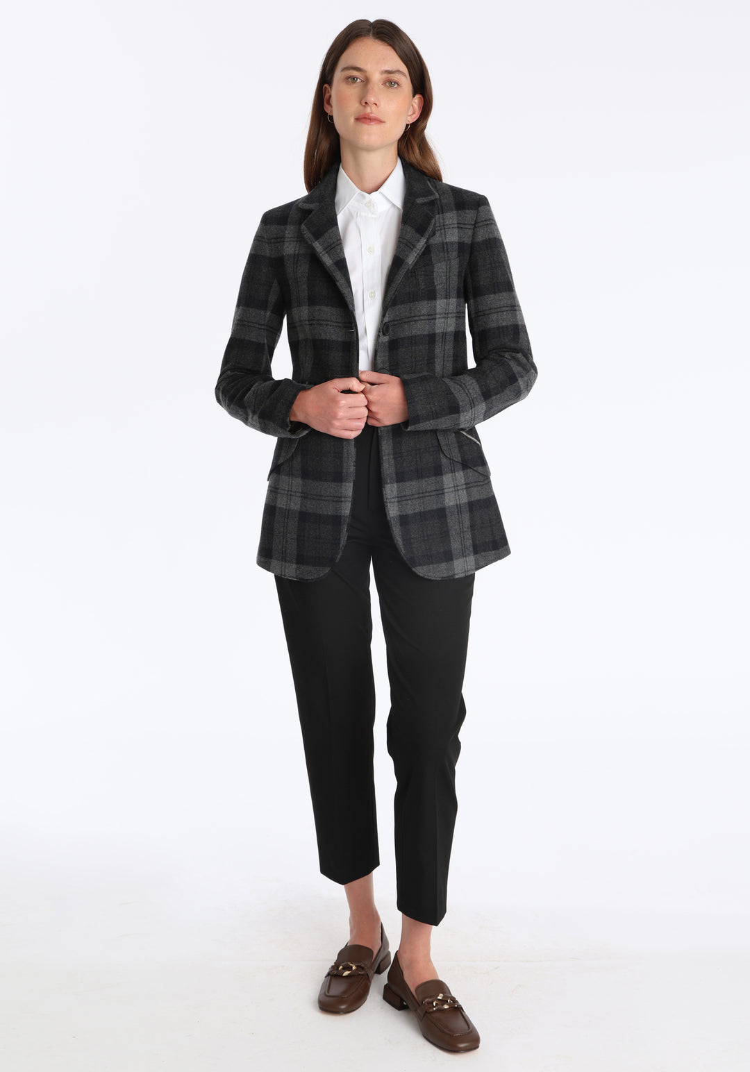 Model wearing the Cass jacket in black and grey tartan cashmere blend with silk velvet trim, a longline, relaxed boyfriend-style jacket with welt pockets, and buttoned collar tab inspired by equestrian tailoring.