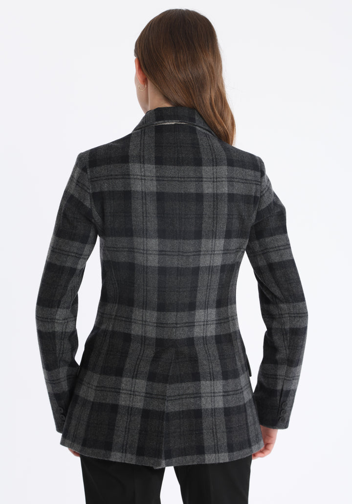 Model wearing the Cass jacket in black and grey tartan cashmere blend with silk velvet trim, a longline, relaxed boyfriend-style jacket with welt pockets, and buttoned collar tab inspired by equestrian tailoring.