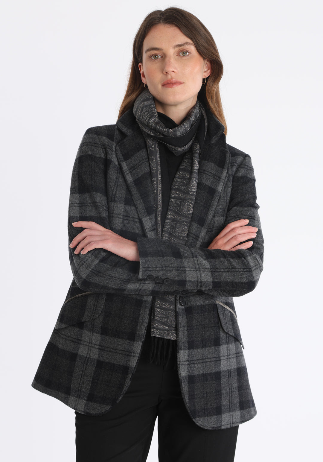 Model wearing the Cass jacket in black and grey tartan cashmere blend with silk velvet trim, a longline, relaxed boyfriend-style jacket with welt pockets, and buttoned collar tab inspired by equestrian tailoring.
