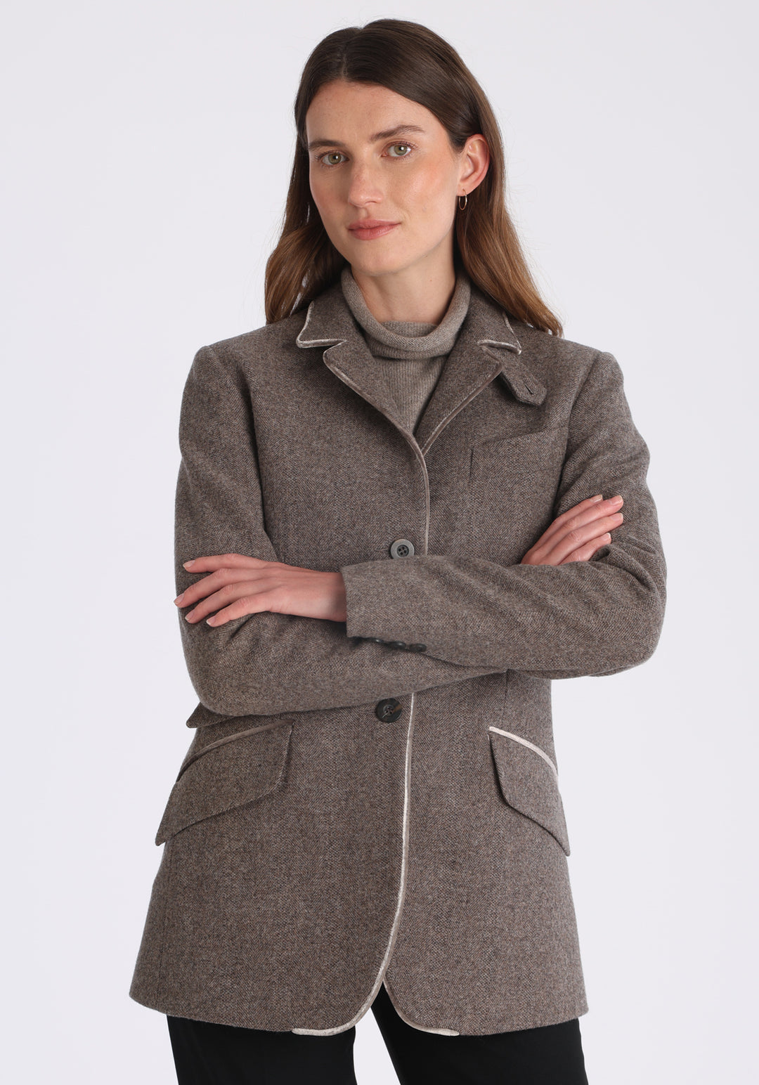 Model wearing the Cass jacket in cool mallow taupe herringbone lambswool with silk velvet trim, a longline, relaxed boyfriend-style jacket with welt pockets, and buttoned collar tab inspired by equestrian tailoring.