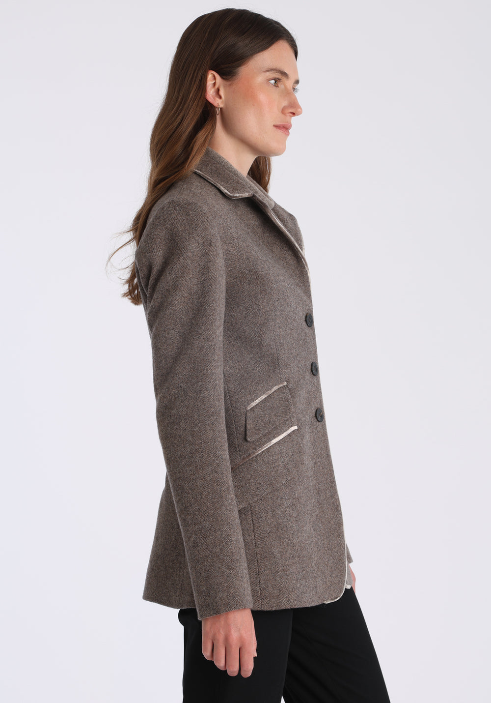 Model wearing the Cass jacket in cool mallow taupe herringbone lambswool with silk velvet trim, a longline, relaxed boyfriend-style jacket with welt pockets, and buttoned collar tab inspired by equestrian tailoring.