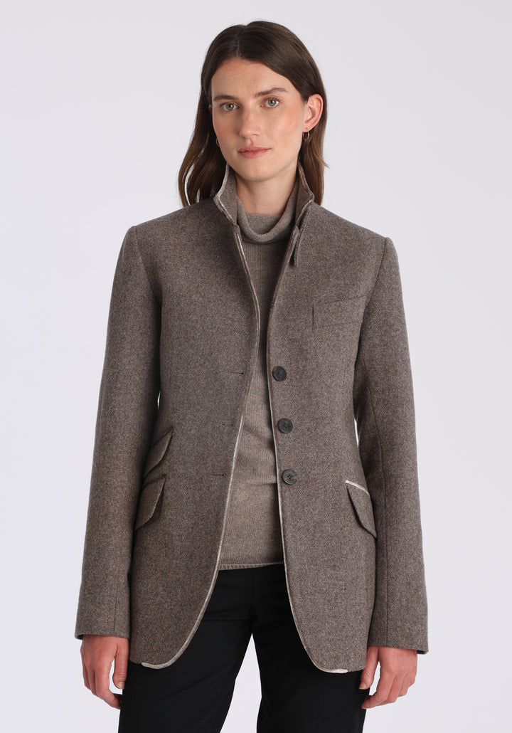 Model wearing the Cass jacket in cool mallow taupe herringbone lambswool with silk velvet trim, a longline, relaxed boyfriend-style jacket with welt pockets, and buttoned collar tab inspired by equestrian tailoring.