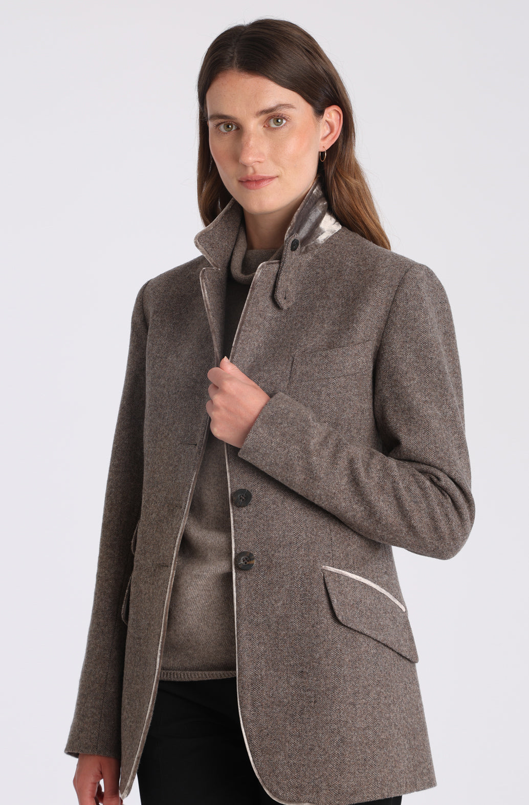 Model wearing the Cass jacket in cool mallow taupe herringbone lambswool with silk velvet trim, a longline, relaxed boyfriend-style jacket with welt pockets, and buttoned collar tab inspired by equestrian tailoring.