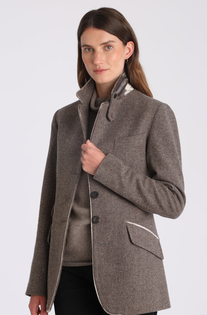 Model wearing the Cass jacket in cool mallow taupe herringbone lambswool with silk velvet trim, a longline, relaxed boyfriend-style jacket with welt pockets, and buttoned collar tab inspired by equestrian tailoring.