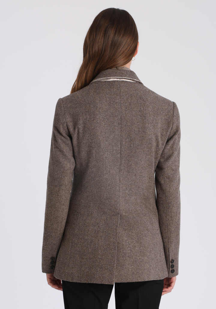Model wearing the Cass jacket in cool mallow taupe herringbone lambswool with silk velvet trim, a longline, relaxed boyfriend-style jacket with welt pockets, and buttoned collar tab inspired by equestrian tailoring.