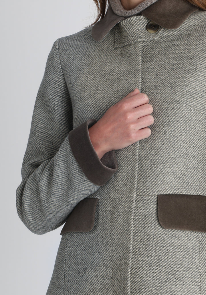 Model wearing the Contrast coat in slate blue and cream twill lambswool with cotton velvet detailing on the collar, cuffs, back belt, and pocket flaps, a longline occasion wear style with a timeless silhouette.