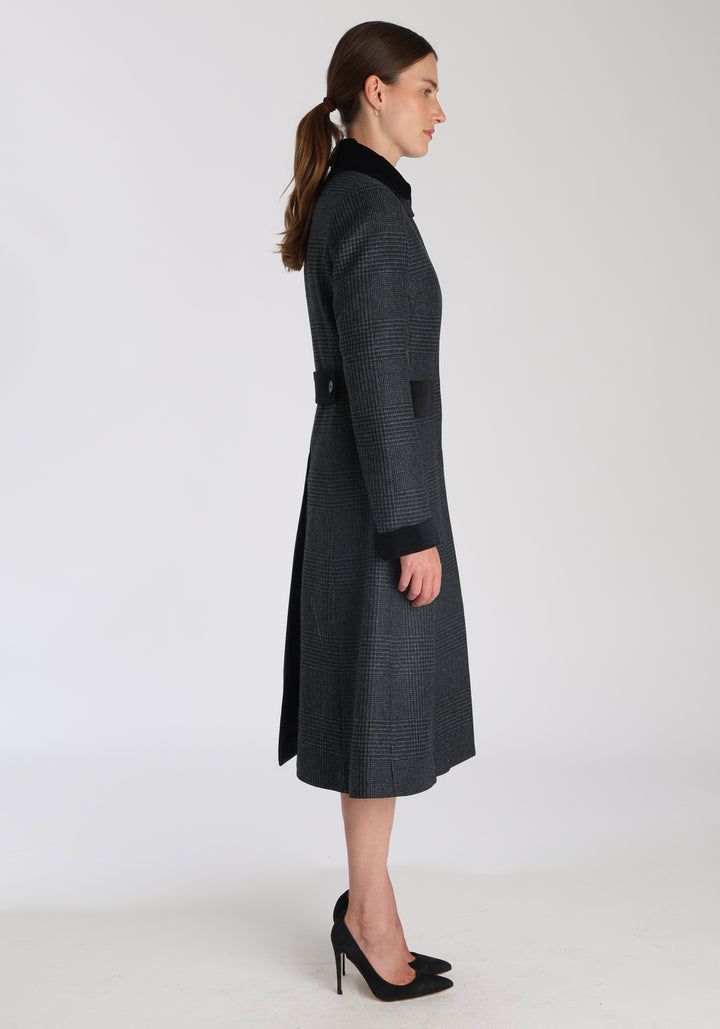 Model wearing the Contrast coat in black and charcoal grey Prince of Wales check merino wool with cotton velvet detailing on the collar, cuffs, back belt, and pocket flaps, a longline occasionwear style with a timeless silhouette.