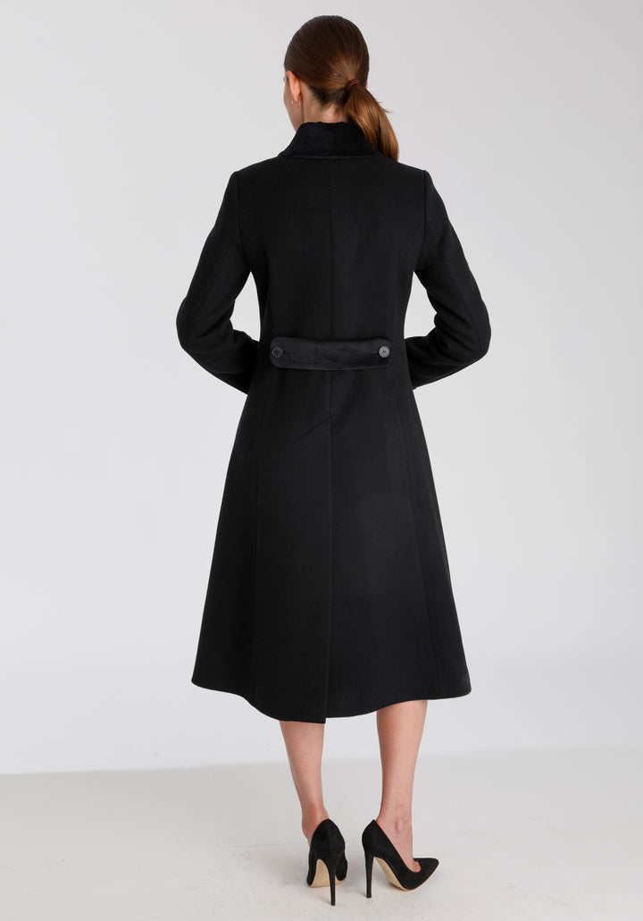 Model wearing the Contrast coat in black wool cashmere with cotton velvet detailing on the collar, cuffs, back belt, and pocket flaps, a longline occasionwear style with a timeless silhouette.