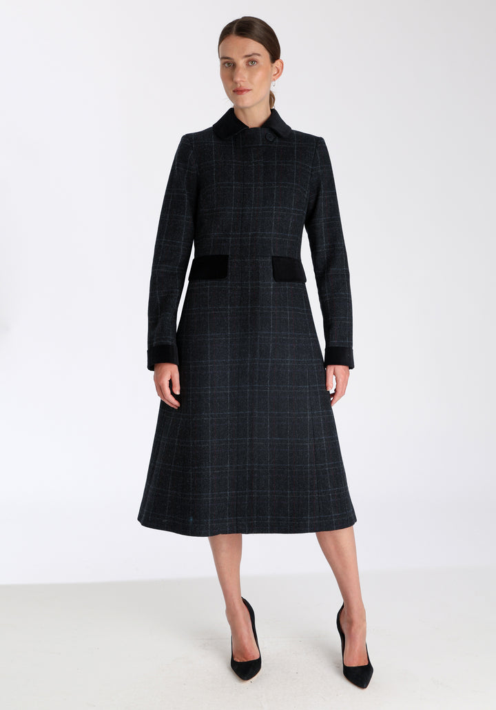 Model wearing the Contrast coat in black with faint overcheck, a long tailored style with black cotton velvet contrasting pockets, cuffs and back belt with a deep back vent for ease of movement.