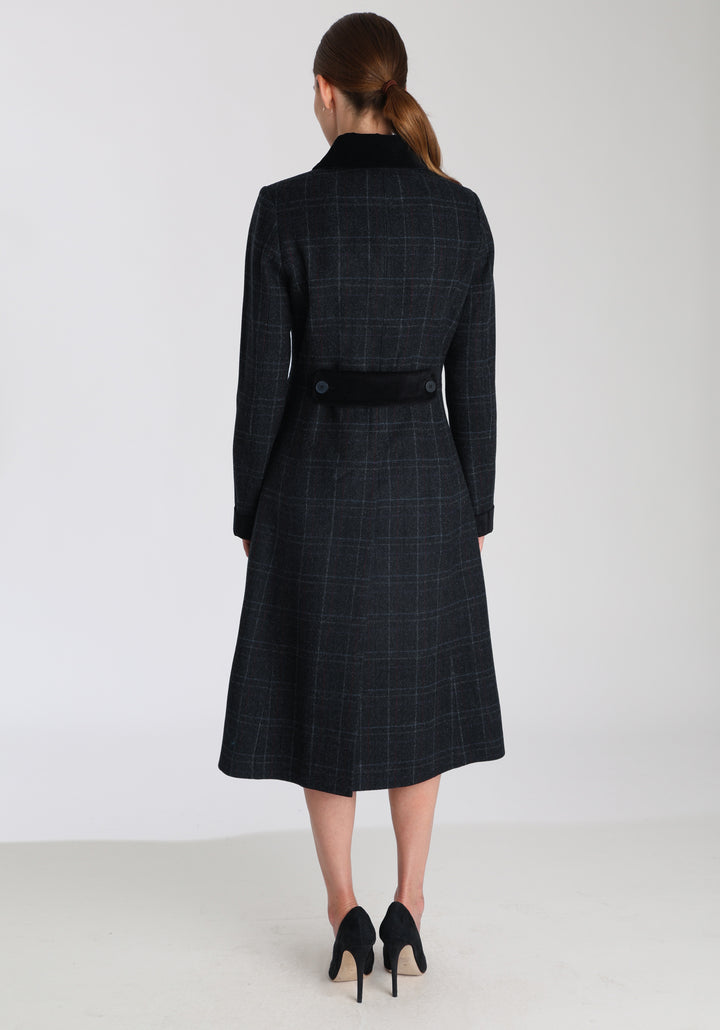 Model wearing the Contrast coat in black with faint overcheck, a long tailored style with black cotton velvet contrasting pockets, cuffs and back belt with a deep back vent for ease of movement.