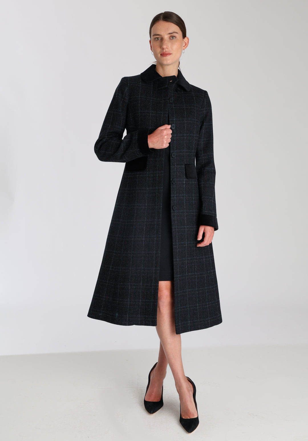Model wearing the Contrast coat in black with faint overcheck, a long tailored style with black cotton velvet contrasting pockets, cuffs and back belt with a deep back vent for ease of movement.