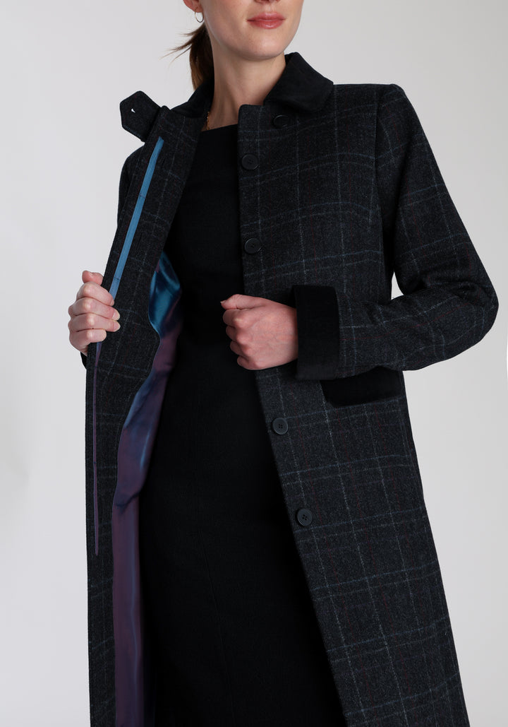 Model wearing the Contrast coat in black with faint overcheck, a long tailored style with black cotton velvet contrasting pockets, cuffs and back belt with a deep back vent for ease of movement.