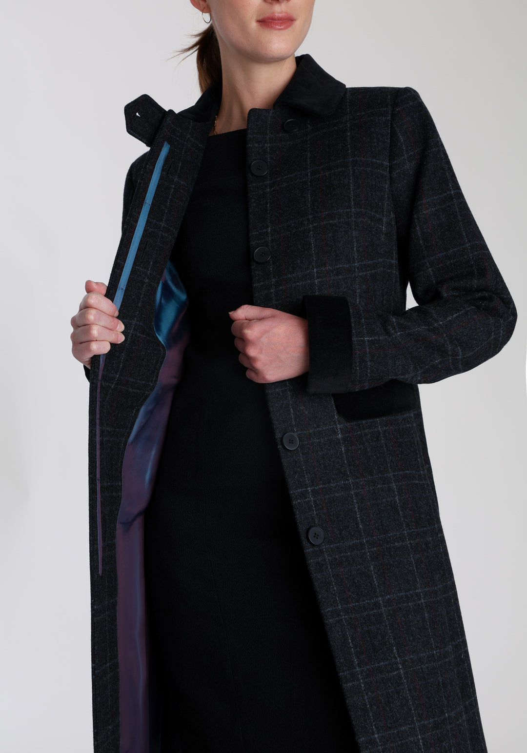 Model wearing the Contrast coat in black with faint overcheck, a long tailored style with black cotton velvet contrasting pockets, cuffs and back belt with a deep back vent for ease of movement.