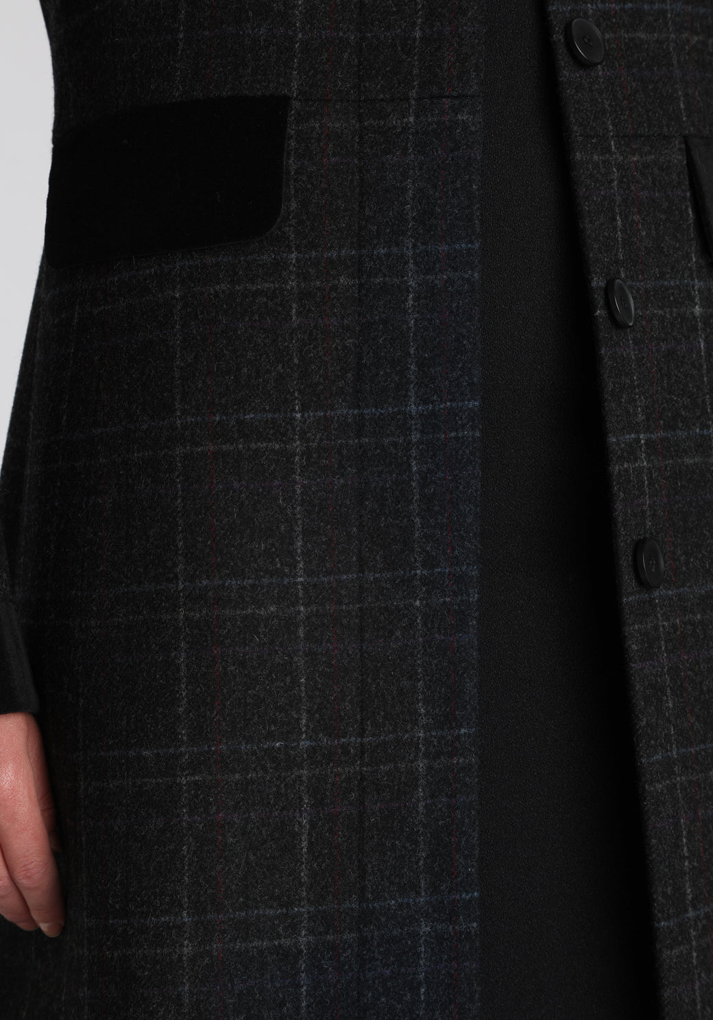 Model wearing the Contrast coat in black with faint overcheck, a long tailored style with black cotton velvet contrasting pockets, cuffs and back belt with a deep back vent for ease of movement.