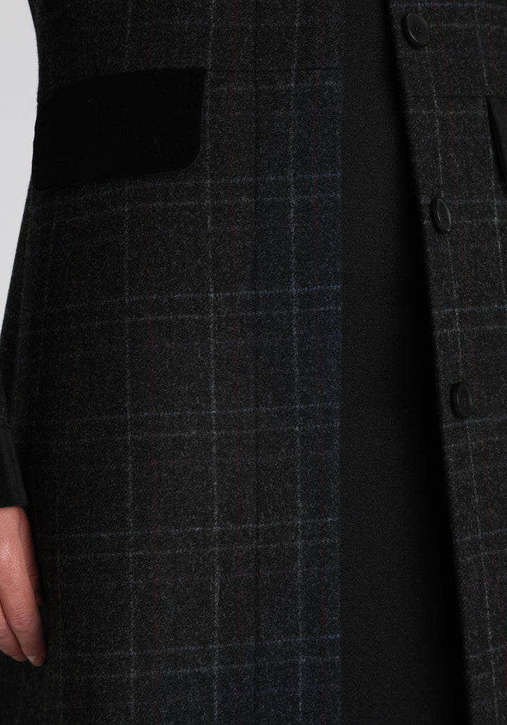 Model wearing the Contrast coat in black with faint overcheck, a long tailored style with black cotton velvet contrasting pockets, cuffs and back belt with a deep back vent for ease of movement.