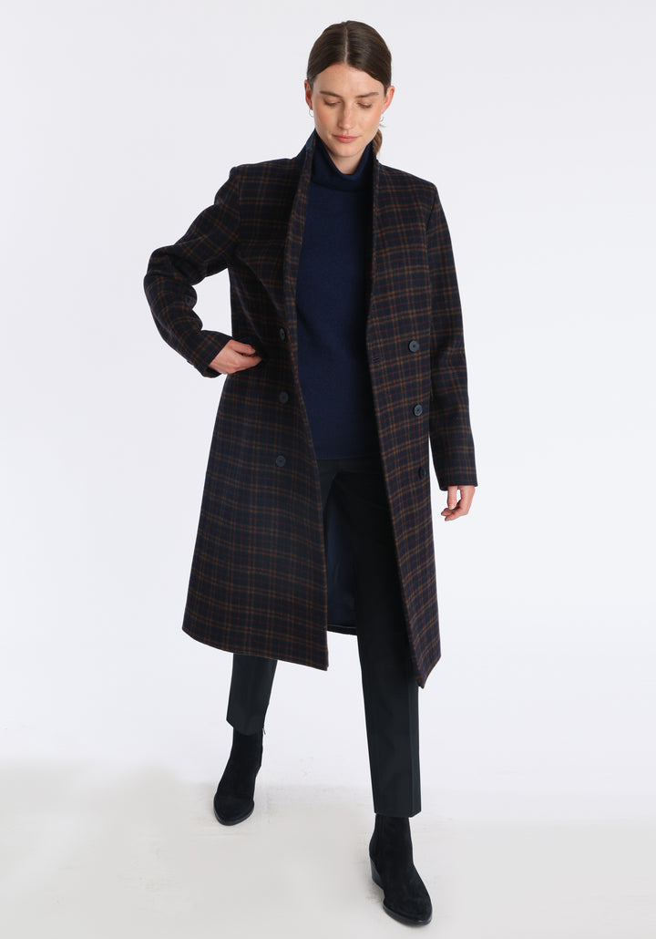 Model wearing the Cully coat in navy and rust check merino wool, a knee-length, double-breasted style with pointed lapels and a structured, straight-cut silhouette designed to flatter.