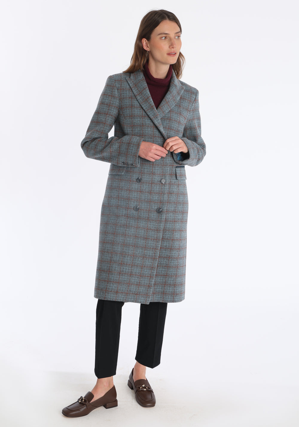 Model wearing the Cully coat in silver and rust check merino wool, a knee-length, double-breasted style with pointed lapels and a structured, straight-cut silhouette designed to flatter.