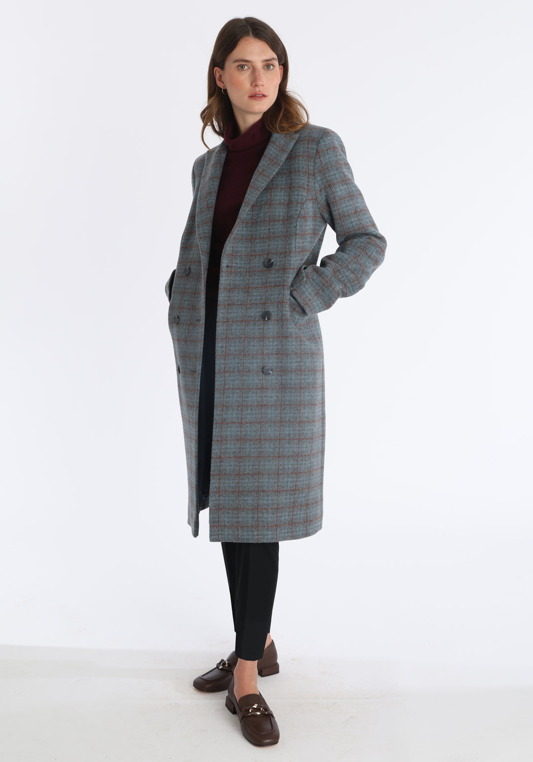 Model wearing the Cully coat in silver and rust check merino wool, a knee-length, double-breasted style with pointed lapels and a structured, straight-cut silhouette designed to flatter.