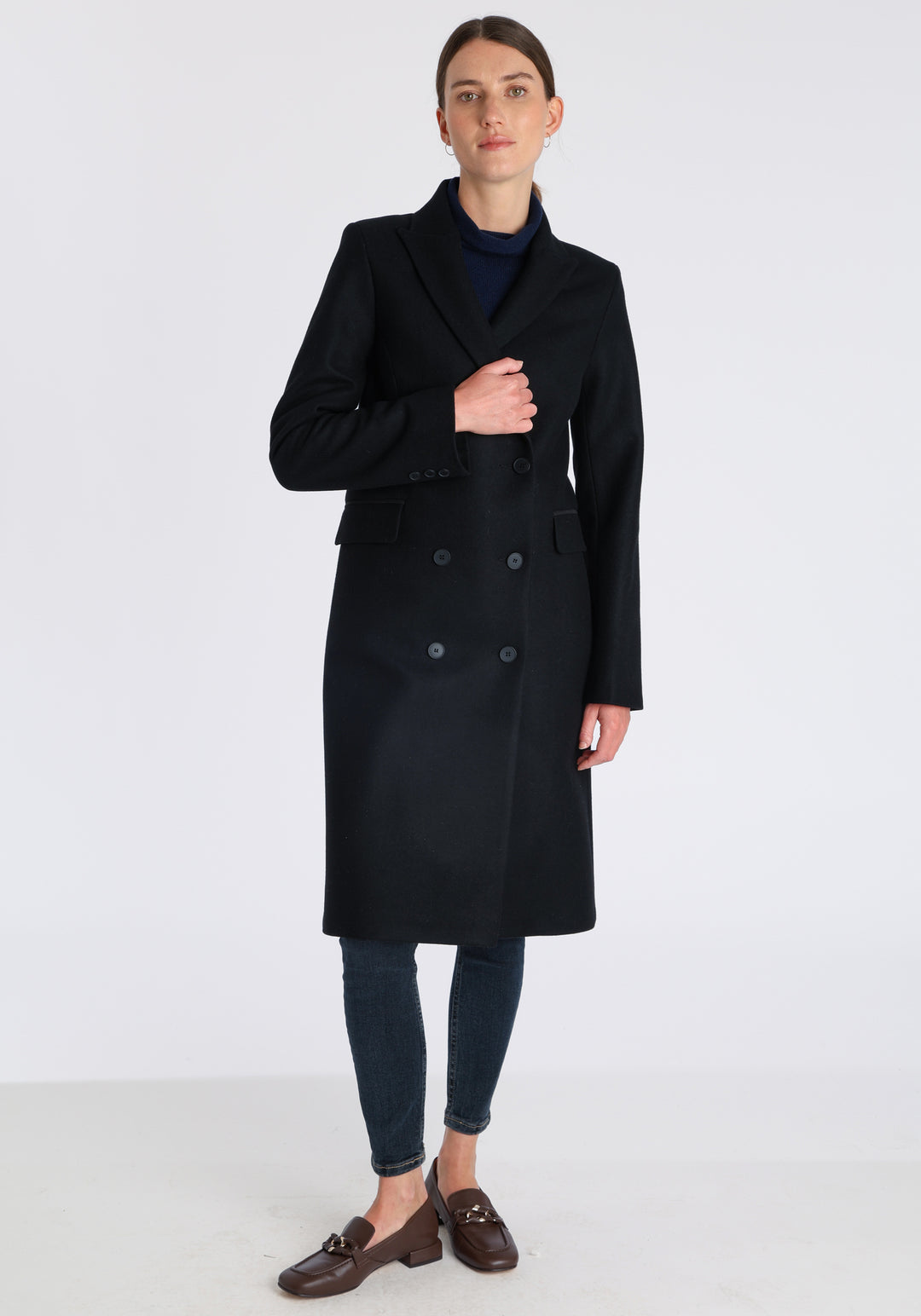 Model wearing the Cully coat in black cashmere blend, a knee-length, double-breasted style with pointed lapels and a structured, straight-cut silhouette designed to flatter.