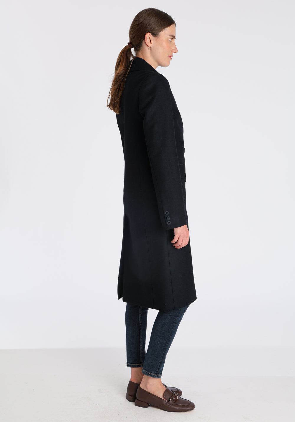 Model wearing the Cully coat in black cashmere blend, a knee-length, double-breasted style with pointed lapels and a structured, straight-cut silhouette designed to flatter.