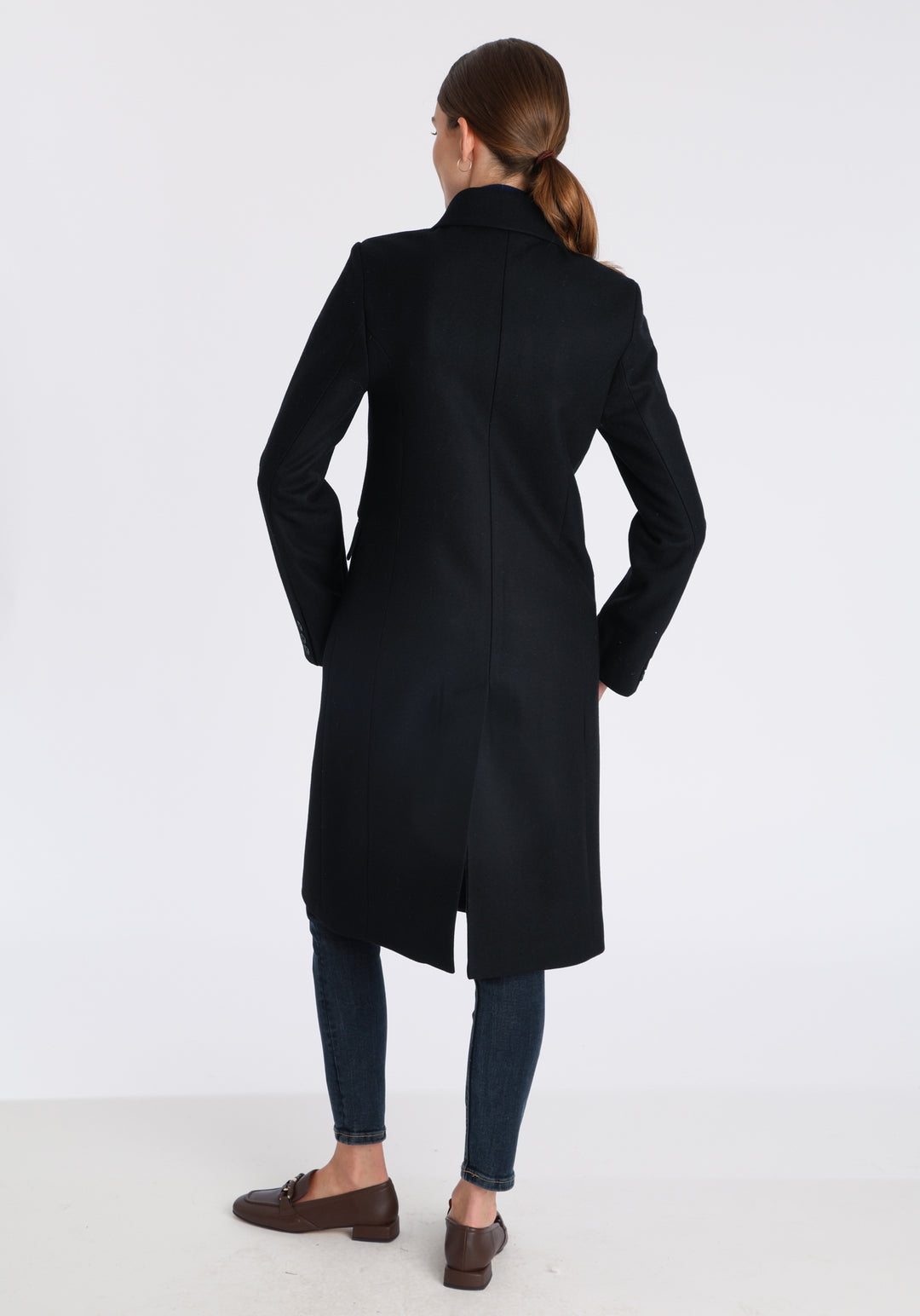 Model wearing the Cully coat in black cashmere blend, a knee-length, double-breasted style with pointed lapels and a structured, straight-cut silhouette designed to flatter.