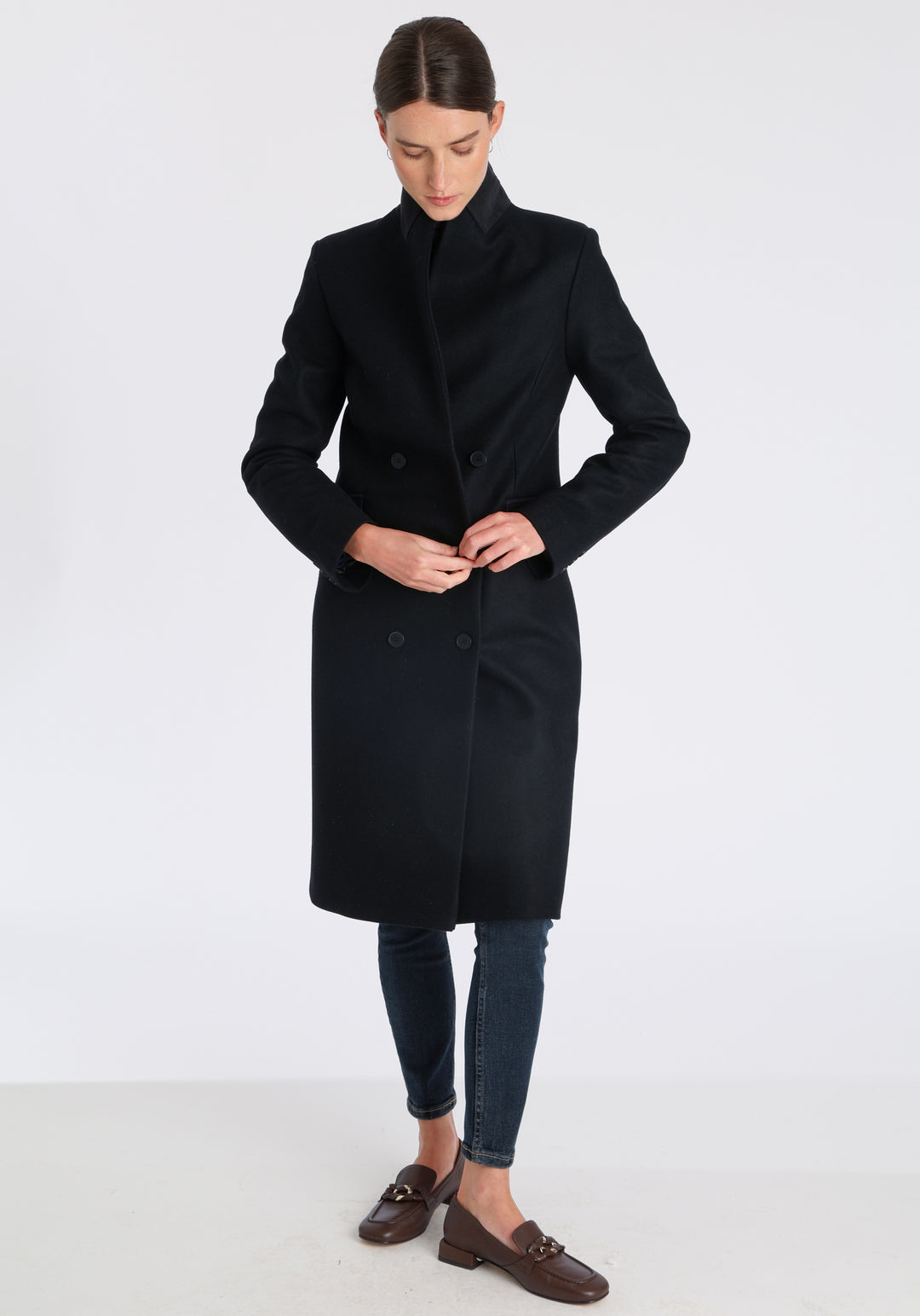 Model wearing the Cully coat in black cashmere blend, a knee-length, double-breasted style with pointed lapels and a structured, straight-cut silhouette designed to flatter.