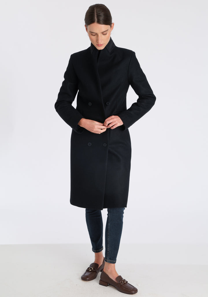 Model wearing the Cully coat in black cashmere blend, a knee-length, double-breasted style with pointed lapels and a structured, straight-cut silhouette designed to flatter.