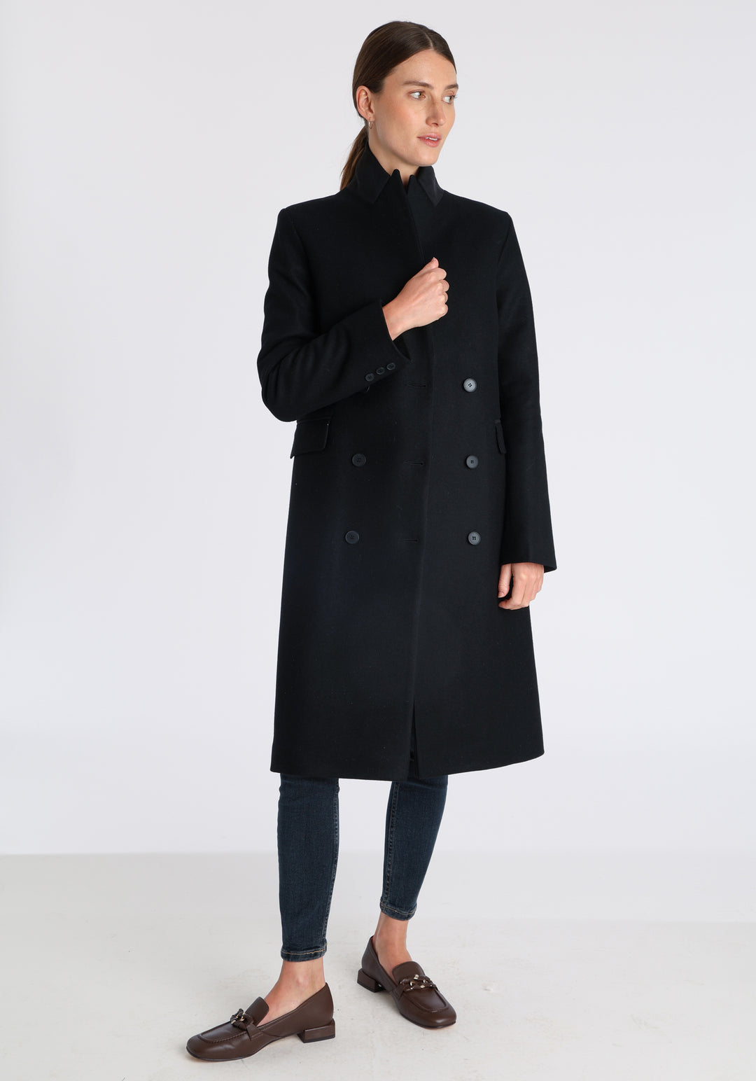 Model wearing the Cully coat in black cashmere blend, a knee-length, double-breasted style with pointed lapels and a structured, straight-cut silhouette designed to flatter.