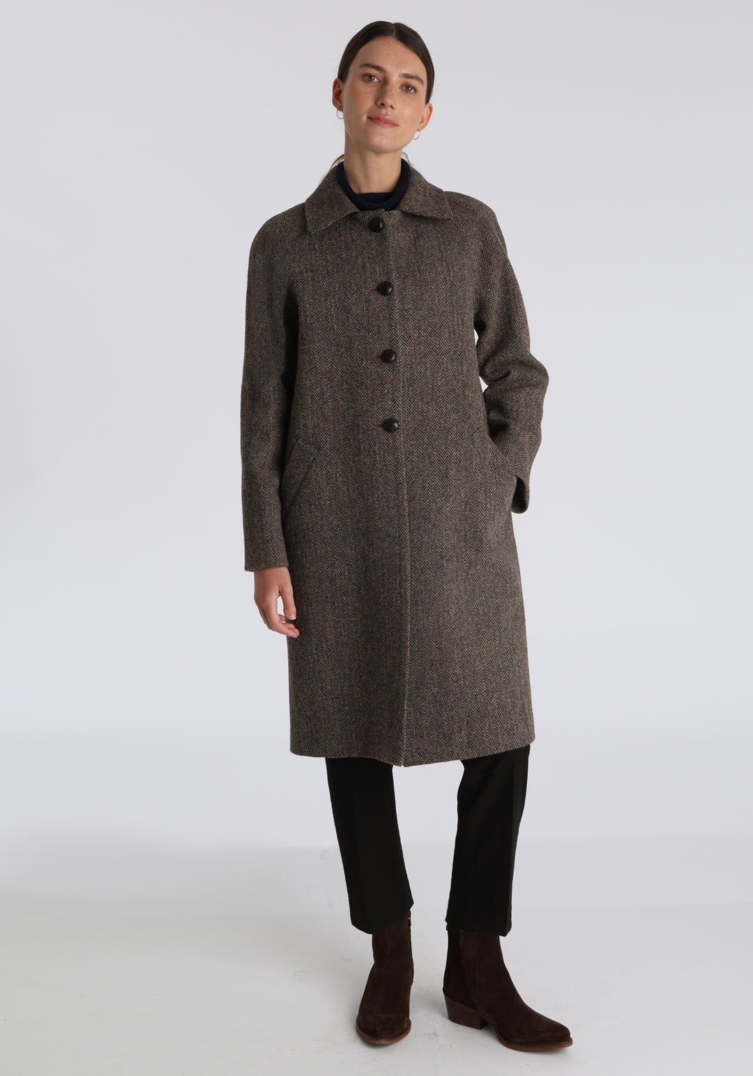 Model wearing the Dari coat in heather herringbone Harris Tweed, a relaxed cocoon-shaped style with raglan sleeves, finished with leather trim.