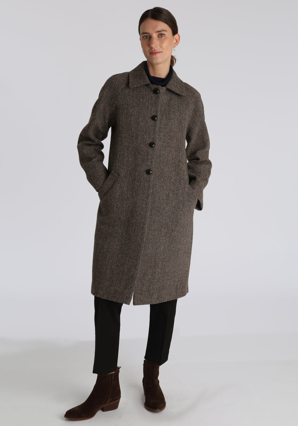 Model wearing the Dari coat in heather herringbone Harris Tweed, a relaxed cocoon-shaped style with raglan sleeves, finished with leather trim.