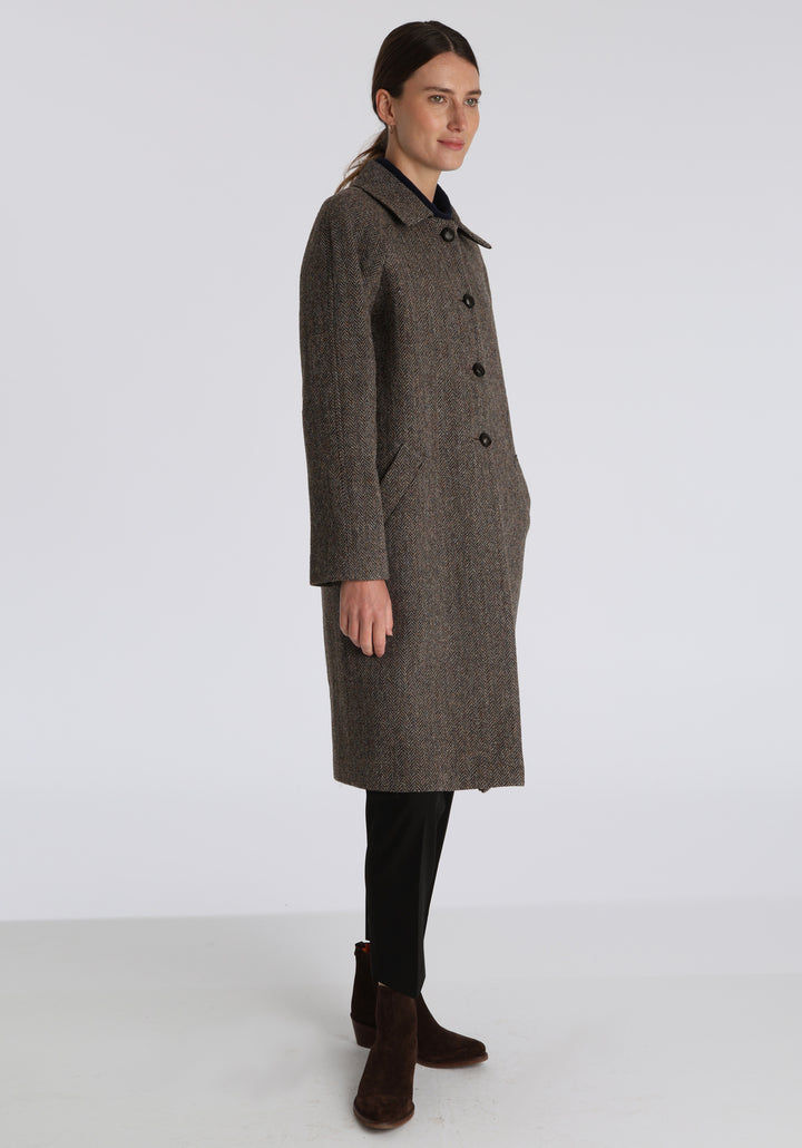 Model wearing the Dari coat in heather herringbone Harris Tweed, a relaxed cocoon-shaped style with raglan sleeves, finished with leather trim.
