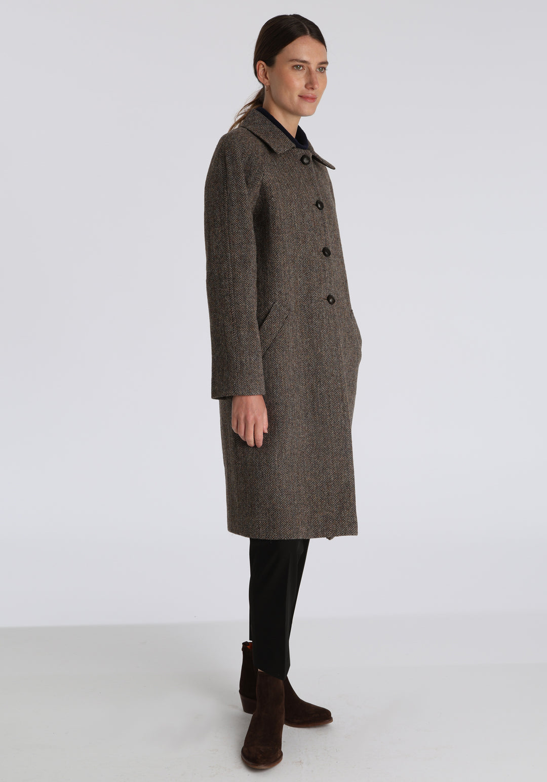 Model wearing the Dari coat in heather herringbone Harris Tweed, a relaxed cocoon-shaped style with raglan sleeves, finished with leather trim.
