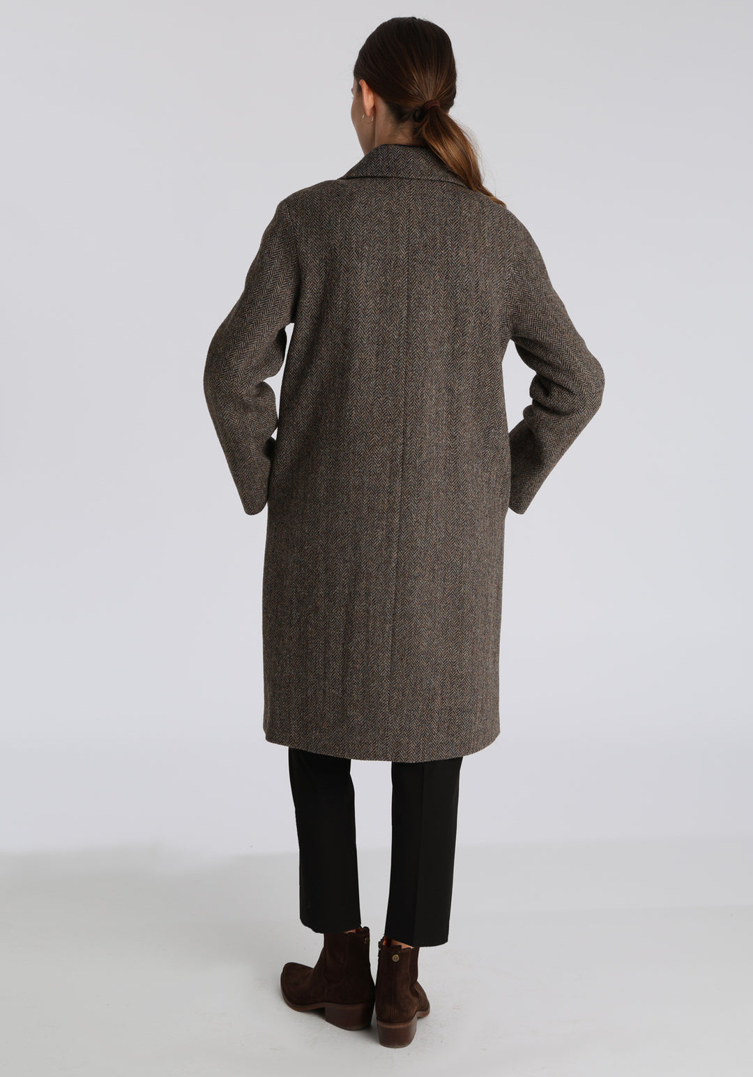 Model wearing the Dari coat in heather herringbone Harris Tweed, a relaxed cocoon-shaped style with raglan sleeves, finished with leather trim.