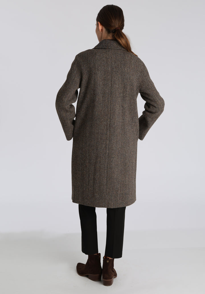 Model wearing the Dari coat in heather herringbone Harris Tweed, a relaxed cocoon-shaped style with raglan sleeves, finished with leather trim.