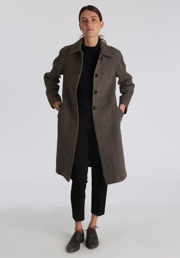 Model wearing the Dari coat in heather herringbone Harris Tweed, a relaxed cocoon-shaped style with raglan sleeves, finished with leather trim.